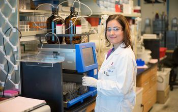 A female researcher holding a test tube stands in front of lab equipment